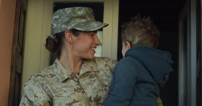 Portrait of Young Happy Female Soldier Holding and kissing her Little Toddler Son After Returning Back Home From a Mission. Mother in Camouflage Military Uniform Showing Affection to her Boy