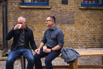 Same sex couple drinking coffee and chatting outside coffee shop