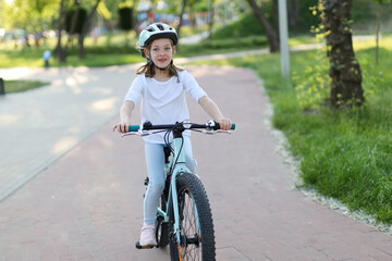 A little girl in a helmet rides a bike path in the park.