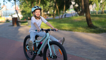 Walking on a bicycle in a summer park, a little girl in a helmet.