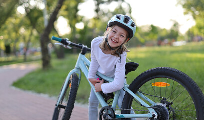 Happy little girl takes out a water bottle from a bicycle in a city park.