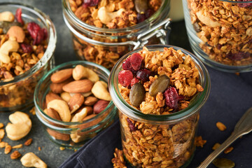 Homemade granola in glass jar with greek yogurt or milk and cashews, almonds, pumpkin with dried cranberry seeds in dark grey table background. Healthy energy breakfast or snack. Top view