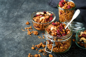 Homemade granola in glass jar with greek yogurt or milk and cashews, almonds, pumpkin with dried cranberry seeds in dark grey table background. Healthy energy breakfast or snack. Top view