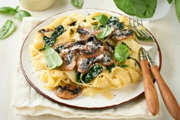 Creamy Alfredo pasta. Italian pasta fettuccini with mushrooms, chicken meat, spinach, basil and cream sauce on white stone or concrete background. Traditional Italian cuisine. Flat lay. Copy space