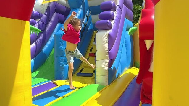 Child jumping on colorful playground trampoline. Kids jump in inflatable bounce castle on kindergarten birthday party Activity and play center for young child. Little girl playing outdoors in summer.