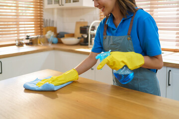 Asian female housewife using table cloth and sprayer in kitchen at home..