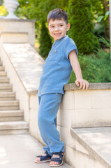 cute kid preschooler boy in casual blue color suit from muslin textile outside in parc posing for...