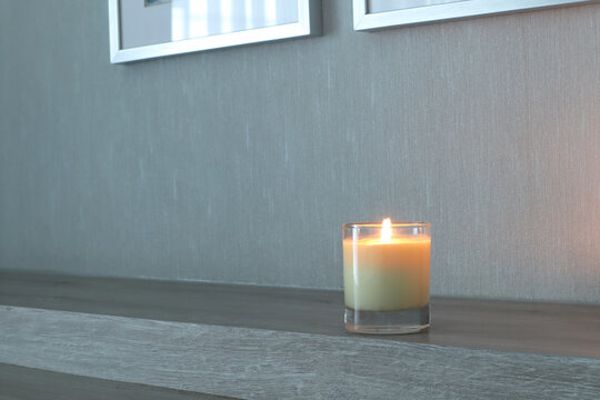 luxury aromatic scented candle glass is displayed on wooden table in the bedroom to create relax and romantic ambient on happy valentine day with background of nice wooden wall and phto frames