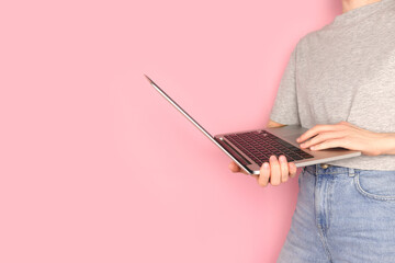 Woman hold in hands laptop. Remote work concept in front of pink pastel background.