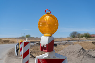 Orange warning light at construction site. Road traffic works safety pole barrier with roadworks...