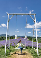 A young girl in a yellow shirt on a swing in a beautiful lavender field. Vertical. Summer mood