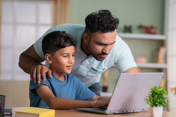 Indian father explaining or teaching from laptop to son at home - concept of family support, home...