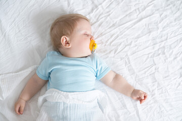 A baby with a pacifier in his mouth is sleeping on the bed