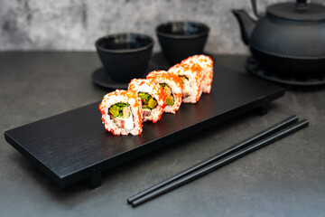 Sushi with red caviar near Japanese cast iron tea pot and cups, with chopsticks, on a black background. Japanese cuisine