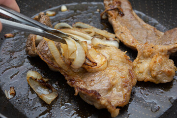 preparing two beef steaks on a frying pan, homemade brazilian cuisine cooking for dinner or lunch with onions..