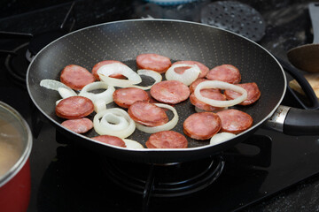 preparing smoked calabrese sausage in a frying pan, frying sausage with onion