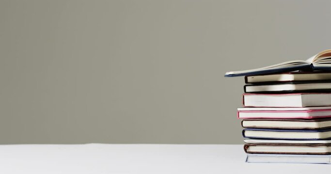 Close up of open book on stack of books with copy space on grey background, in slow motion