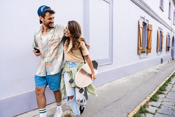 Portrait young couple with skateboard and longboard having fun outdoors. Man and woman skateboarders world travelers tourists in Mediterranean driving and skateboarding through touristic destinations