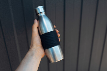 Male hand holding a steel thermo water bottle on metal background with lines of black color.