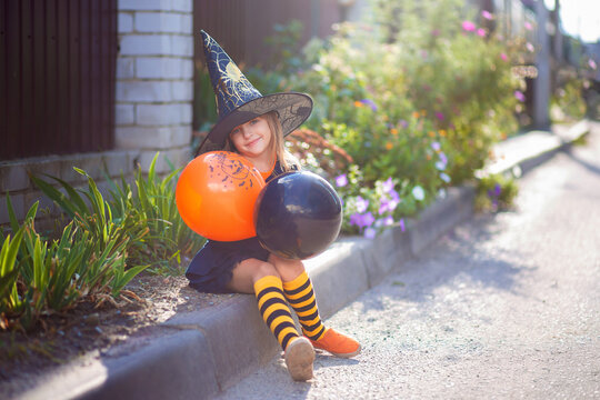 A little girl in a witch costume and with balloons for Halloween walks down the street and rejoices in the holiday