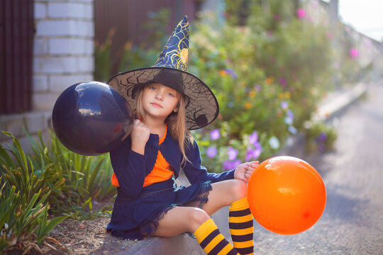 A little girl in a witch costume and with balloons for Halloween walks down the street and rejoices in the holiday
