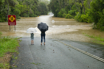 Two people in front of a flooded road in the Sunshine Coast, Queensland, Australia.