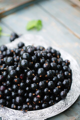 Ripe black currants in a vintage metal tray on a wooden background.
