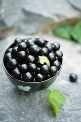 Ripe black currants in a black bowl on a stone background