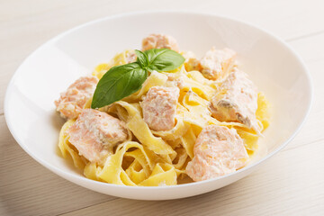 Fettuccine pasta with salmon in cream sauce on white plate on wood table close up. Mediterranean cuisine.
