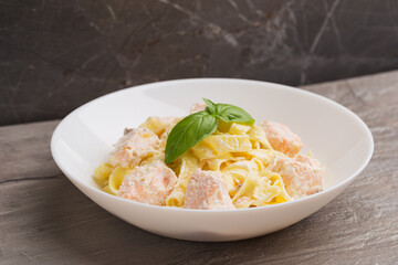 A view of a plate of Fettuccine pasta with salmon in creamy sauce on dark table. Mediterranean cuisine.  Isometric style.