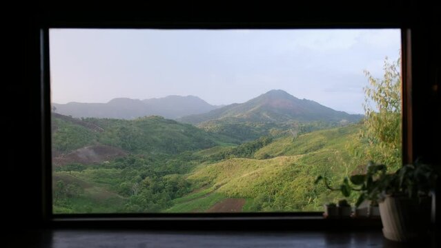 Landscape image of trees blowing in the wind and a beautiful greenery mountains view through the window
