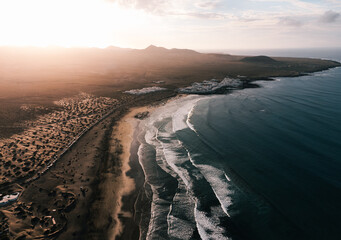 Aerial photo of sunset on Caleta de Famara in Canary Islands - Lanzarote:  wide photo from above with strong waves in blue ocean and sunset on sky. Cliffs and rocks with ocean by drone.