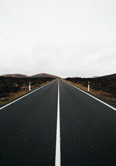 Vertical image of empty road with perfect symmetric lines at overcast day. Travel shot from trip of Lava island - Lanzarote (Canary Islands).