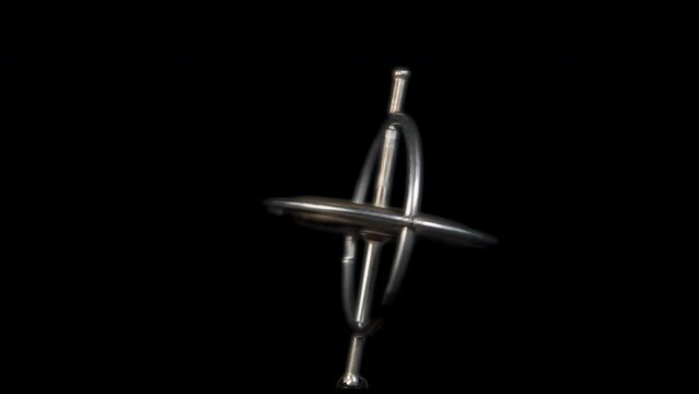 A spinning metal giroscope slowing down with a black background.