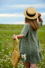 A young woman in a straw hat  on a chamomile field. Happy lady and nature - the concept of harmony. The idea of self-care, healthy lifestyle and positive