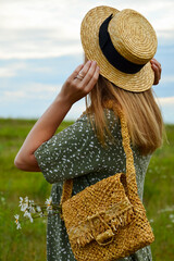 A young woman in a straw hat and with a straw bag on a chamomile field. Happy lady and nature - the concept of harmony. The idea of self-care, healthy lifestyle and positive