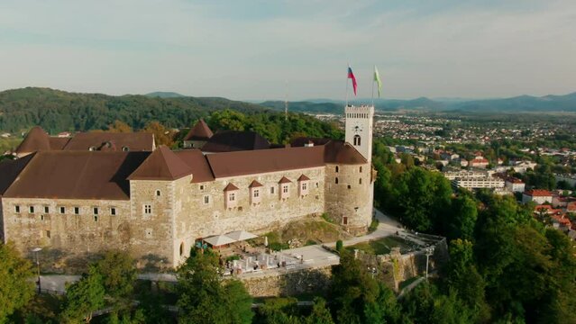 Aerial view of Ljubljana Castle in capital of Slovenia, Central Europe, EU. Medieval Fortress with flags on green Hill in old downtown as a key landmark. Sightseeing and travel. 4k drone orbit shot