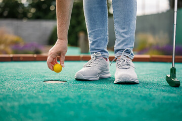 Woman plays mini golf and taking ball out from the hole after successful putting