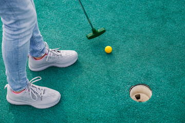 Woman playing miniature golf and trying putting ball into hole. Summer leisure activity