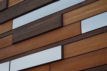 Building wall. Finishing with decorative brown wood and mirror panels. Beautiful abstract wooden background.