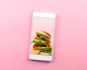 Top view smartphone with burger on screen, pink background. Online food delivery application concept.