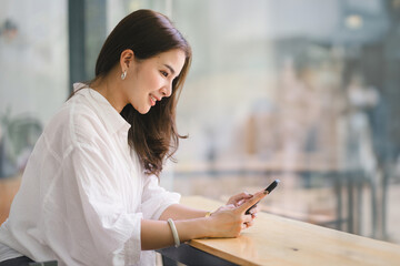 Beautiful young millennial Asian woman using a smartphone at a cafe. Portrait of a gorgeous smiling...