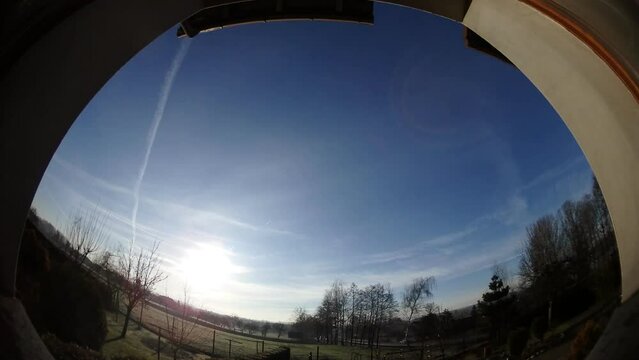 Panorama 204 time lapse - one day from sunrise to sunset. Window view with short day in winter. Sun low on horizon, snow, trees, blue sky, halo, moving clouds.