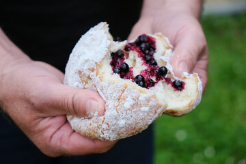 Donut or ponchik in male hands. Traditional donut with blueberries. Sugar powder. Local small food...