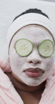 Vertical video close up of african american woman in beauty face mask with cucumber slices on eyes