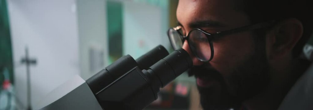 Close Up Face Man Scientist With Glasses Looking Under A Microscope In A Light Laboratory. Medicine, Biotechnology, Chemistry