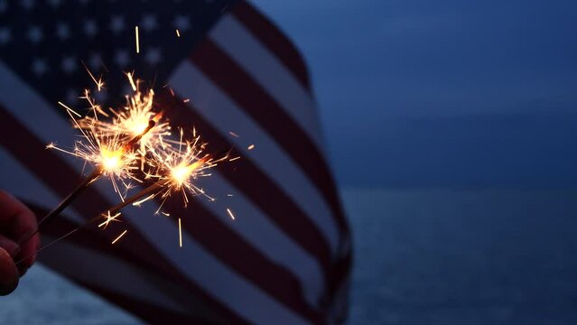 Fourth of July celebration with a hand holding sparklers and pyrotechnics on an American flag background. Concepts Fourth of July, Holiday, United States, Independence, Memorial, Veterans Day