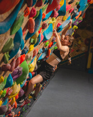 Sportwoman climber climbing steep boulder wall, climbing on artificial wall indoors. Extreme sports and bouldering concept.