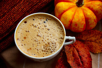 A cup of cappuccino coffee, orange pumpkins and knitted brown clothes on the windowsill. Warm and...