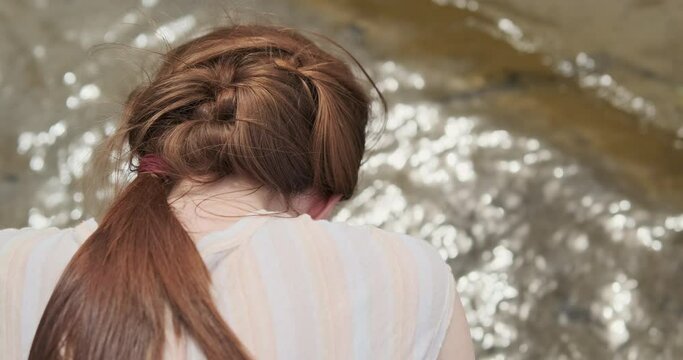 Woman examines the surface of the river water, close-up, rear view. Reflection of the sun in the waves of the river.